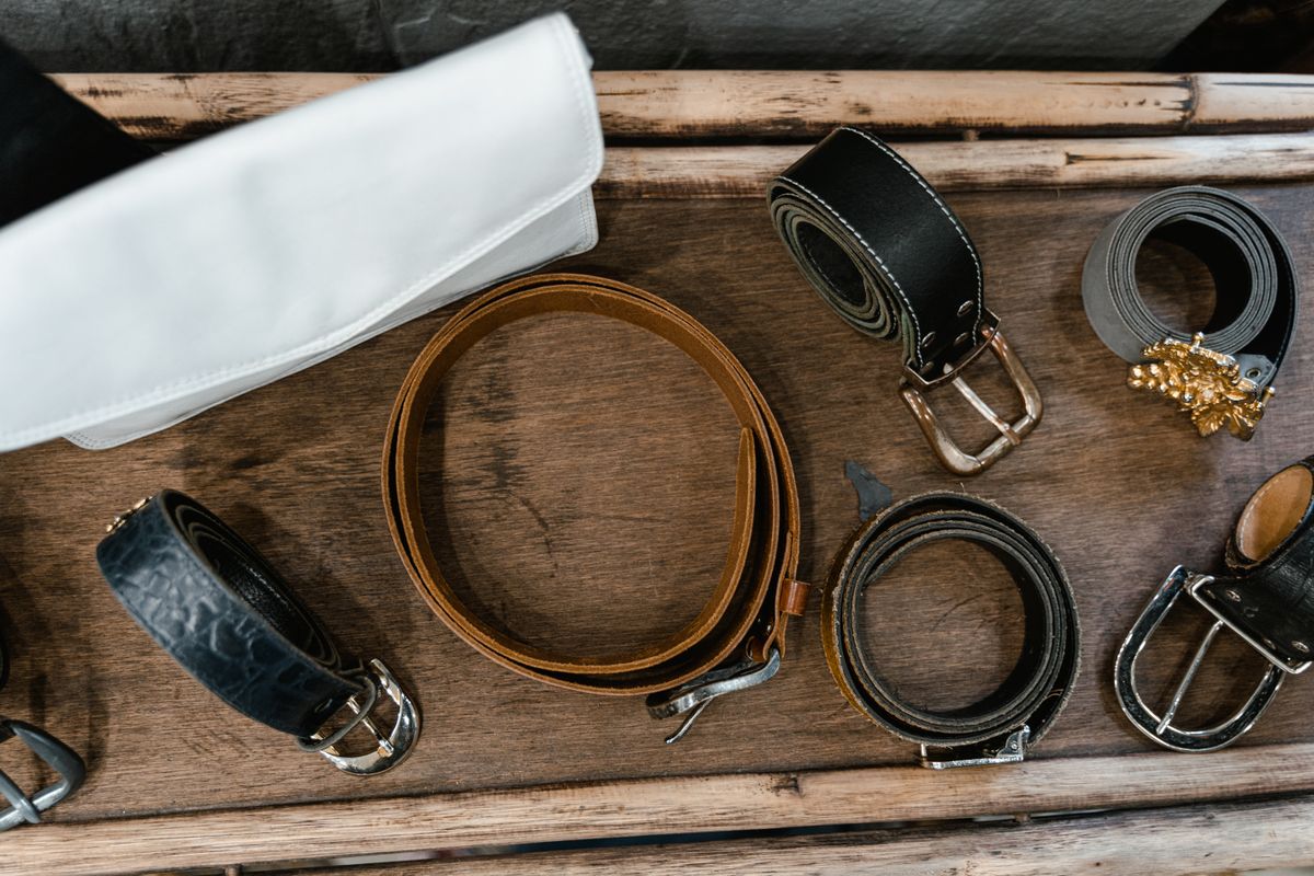 Leather belts with metal buckles laid out on a wooden table