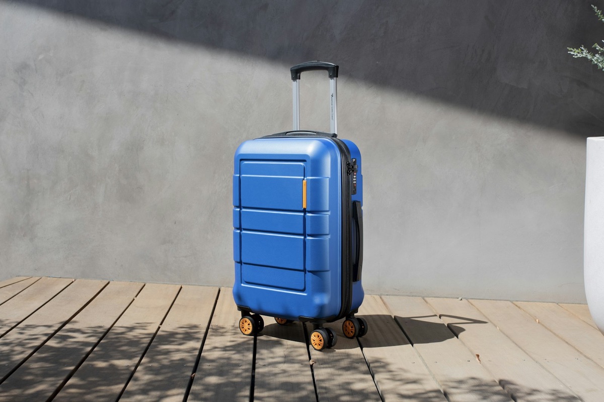 A blue hard-shell carry-on on a wooden deck with its handle extended and wheels visible
