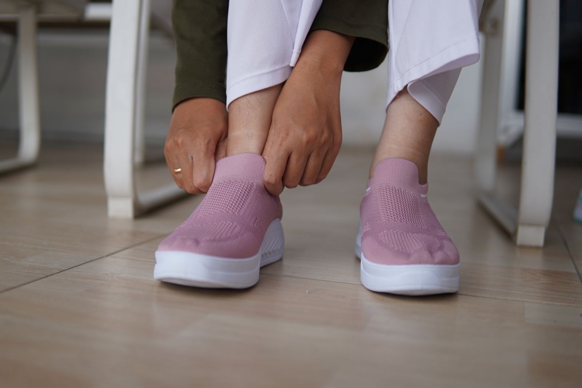 A person pressing a finger around the heel collar of a slip-on sneaker while trying it on