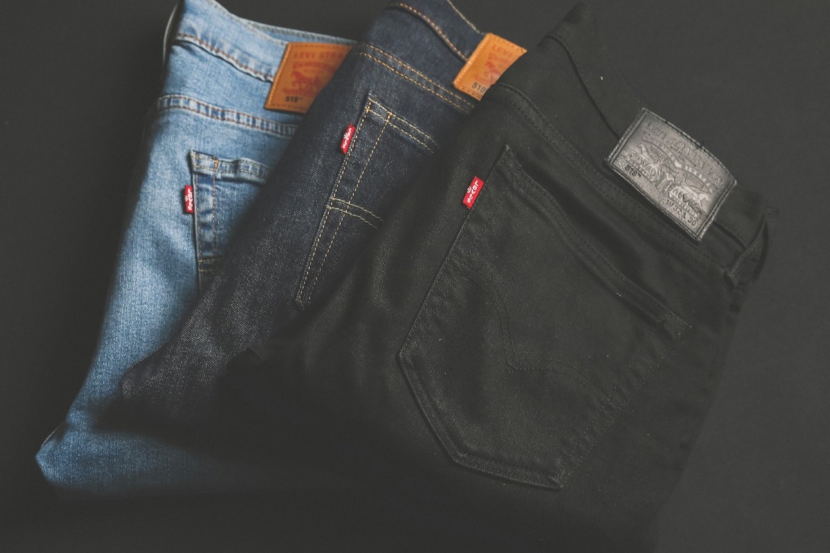 Three pairs of jeans in light, dark and black denim fanned out on a dark surface