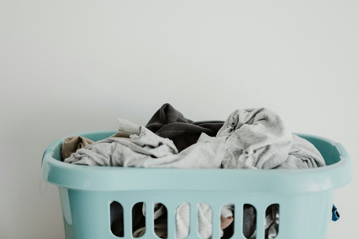 A laundry basket filled with light and dark clothes against a white wall