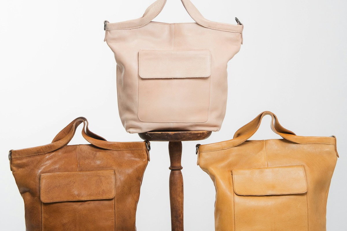 Three leather shoulder bags in tan and cream standing on a wooden stand