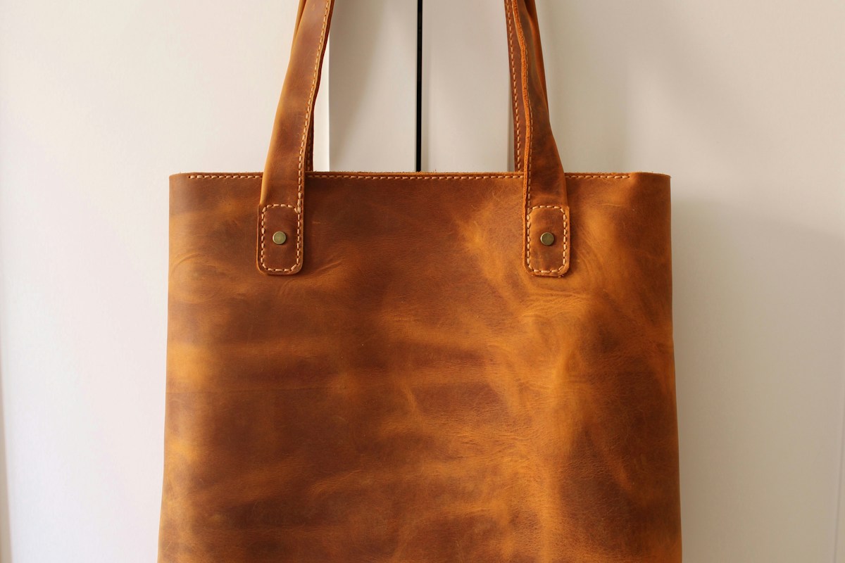 A brown leather shopper tote hanging against a white wall