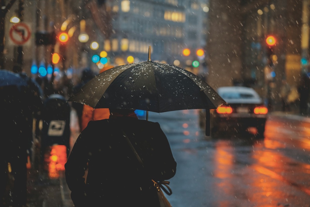 A person holding a black umbrella on a rainy city street at dusk