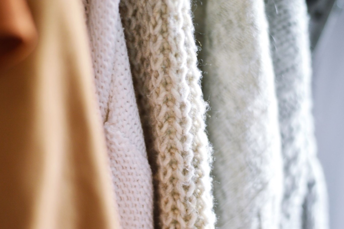 Several knitted sweaters in cream and beige tones hanging side by side on a rail