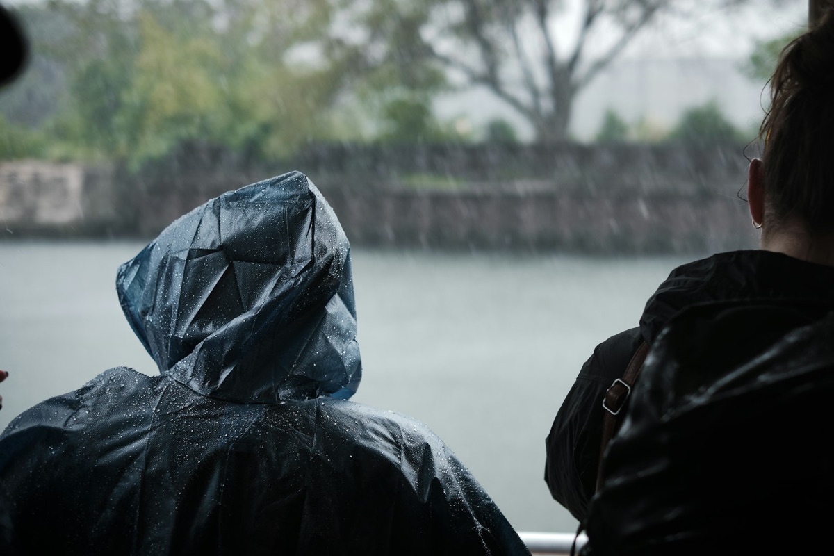 Two people in hooded rain jackets looking out over water in heavy rain