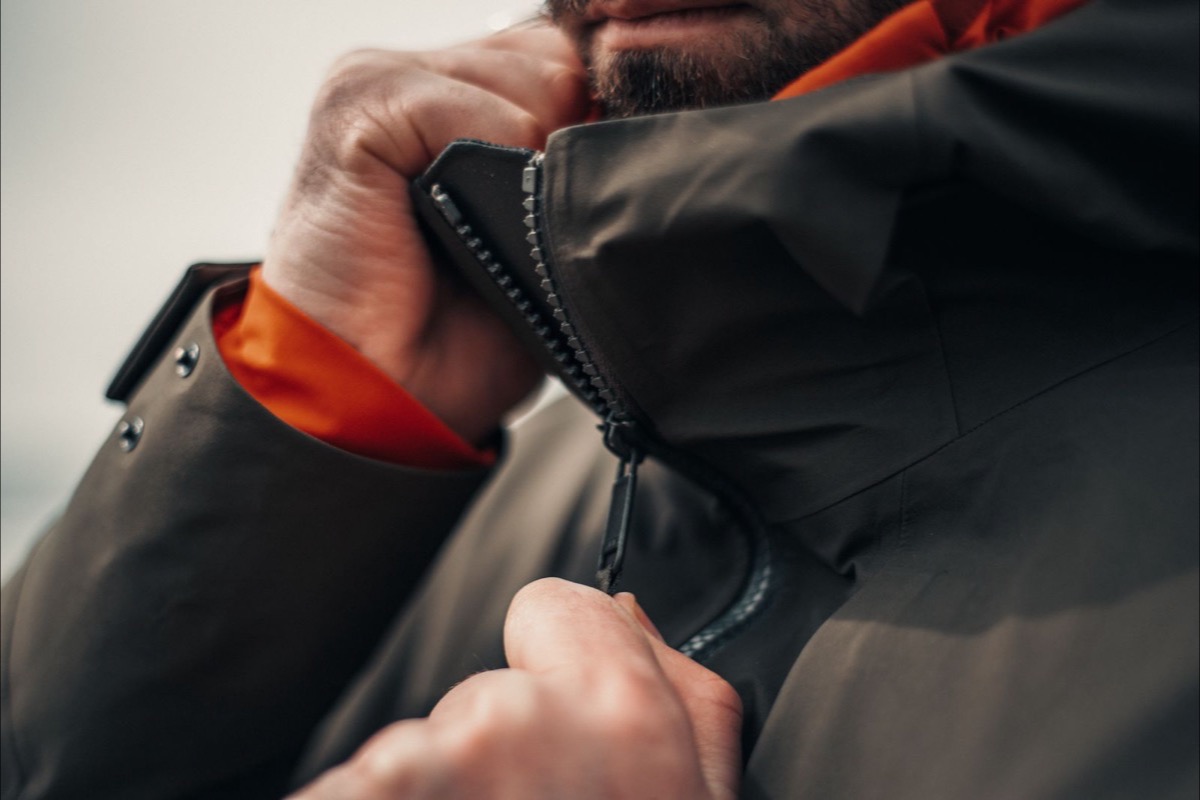A close-up of hands zipping up the front zip of a dark technical outdoor jacket